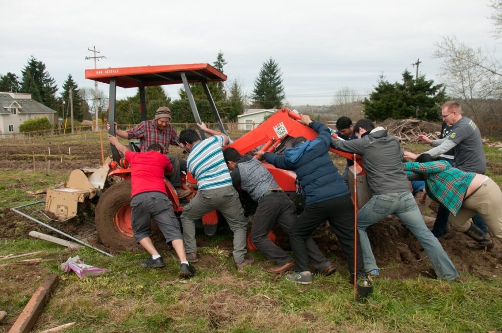 Volunteers help free tractor from muddy path.