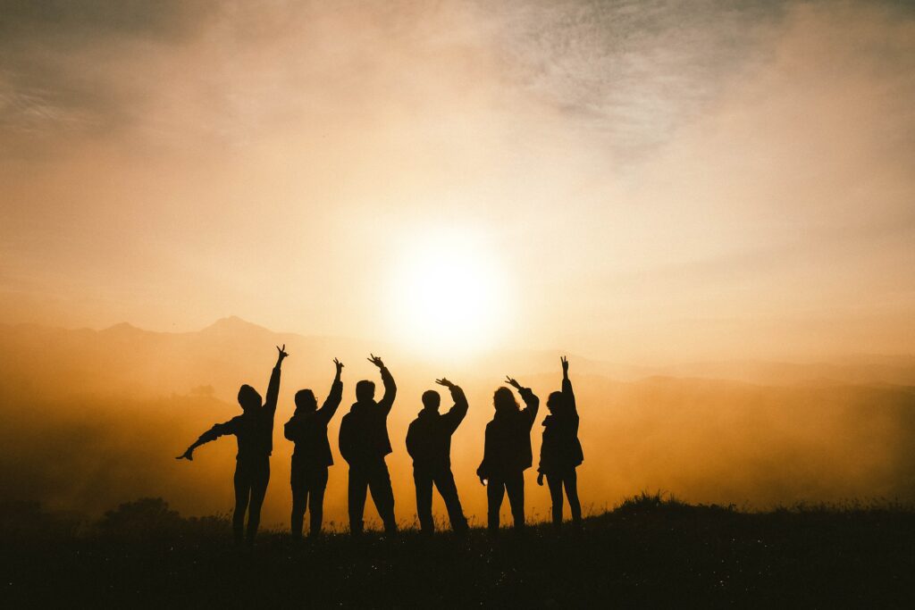 people with their hands raised with the sun behind them