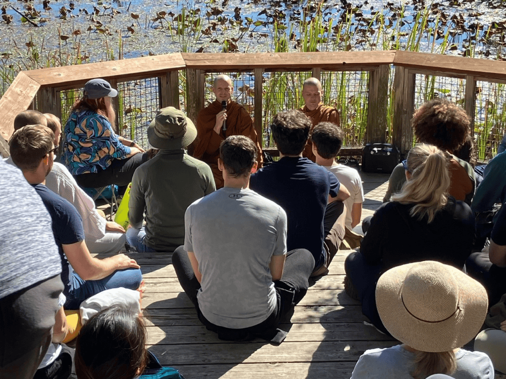 A photo of 2 monks and more people meditating in the outdoors.