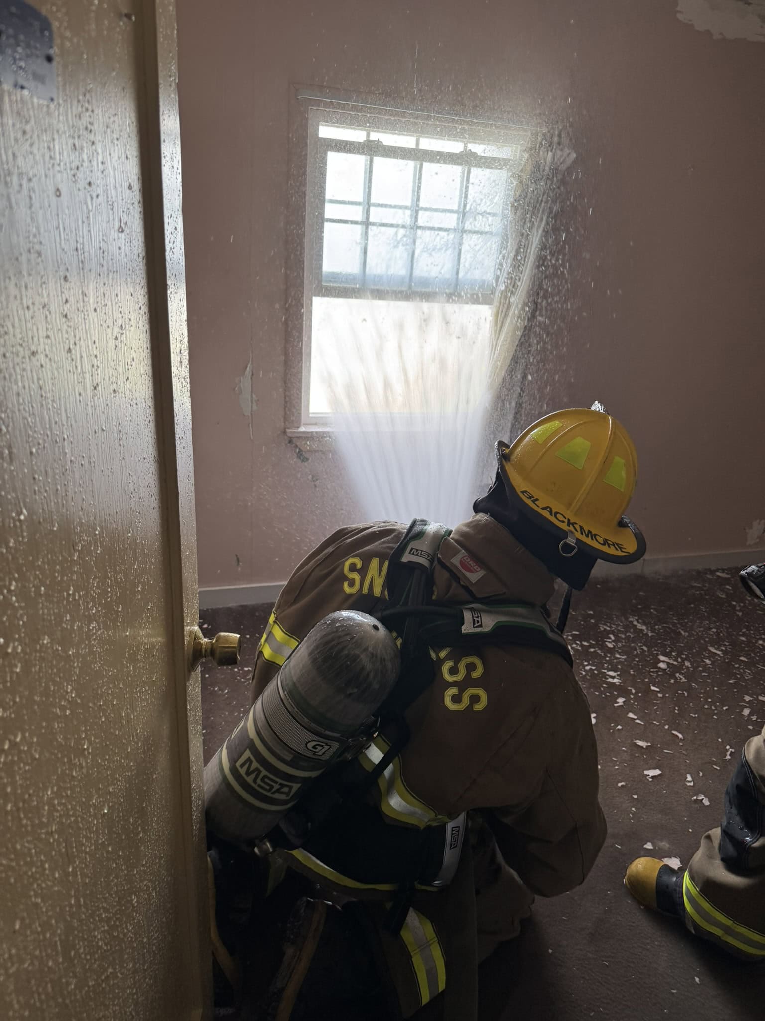 Firefighter inside spraying water through window.