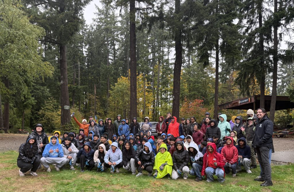 A group of people sitting on grass with trees in the background