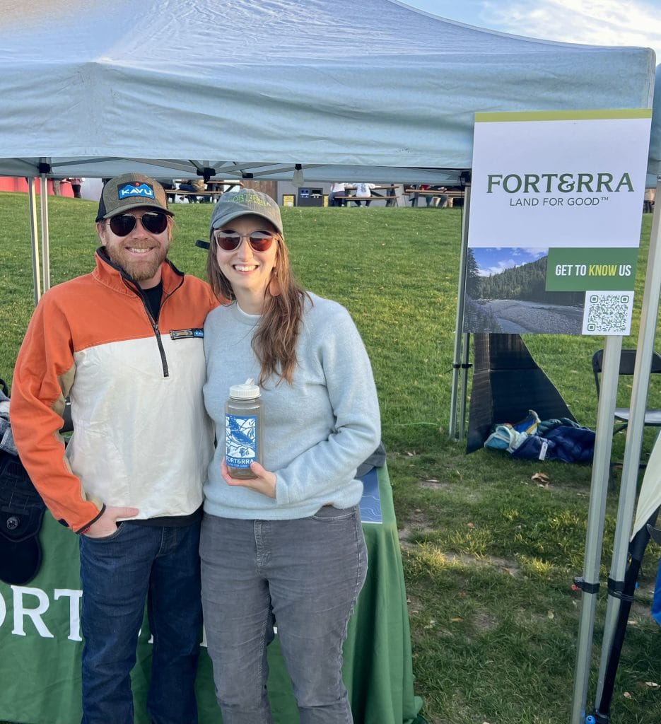 Two ticket winners stand beside the Forterra booth and event signage at the All At Once Village Green at The Gorge Amphitheatre.